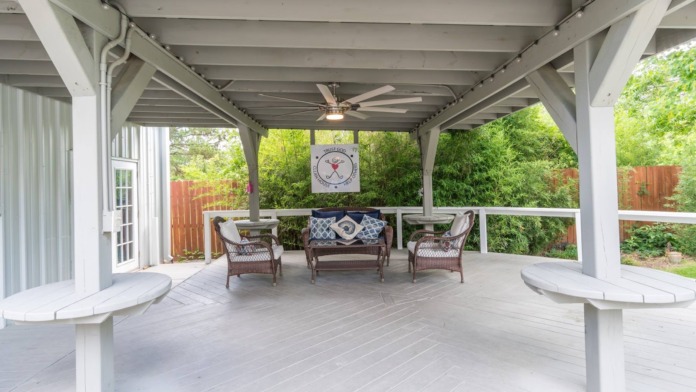 Exterior covered patio with comfortable seating, clock, and garden views surrounded by mature trees