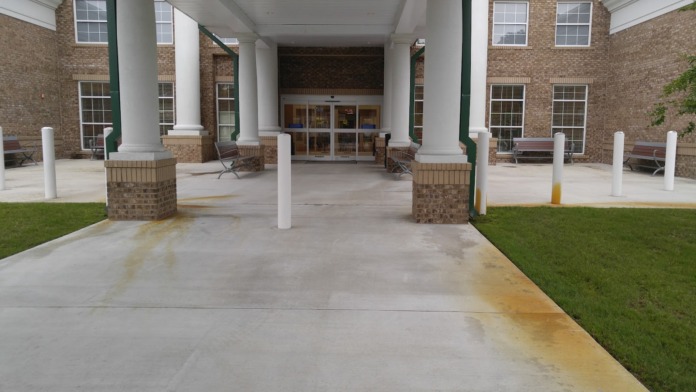 Exterior covered patio with white columns, brick building facade, benches, and manicured grounds
