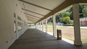 Interior covered walkway with white columns, dark tile flooring, and views to outdoor grounds and buildings
