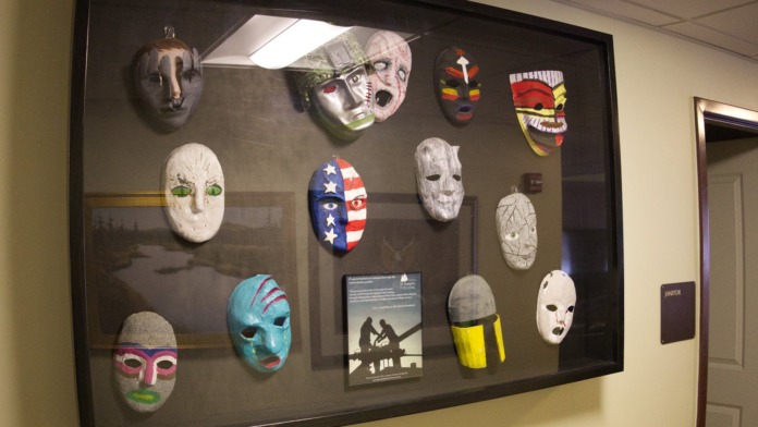 Interior wall display featuring decorative masks from various cultures and historical items in a framed exhibition case