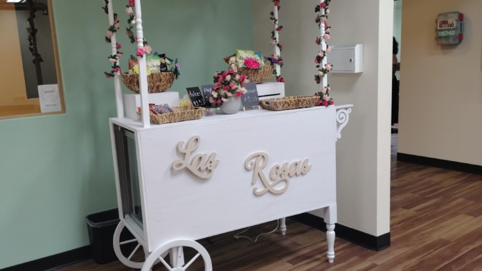 Interior view of decorated white serving kiosk with floral arrangements and signage labeled Lila Rosas