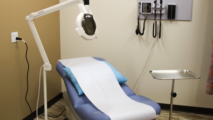 Interior dental treatment room with patient chair, overhead operatory light, and wall-mounted diagnostic equipment