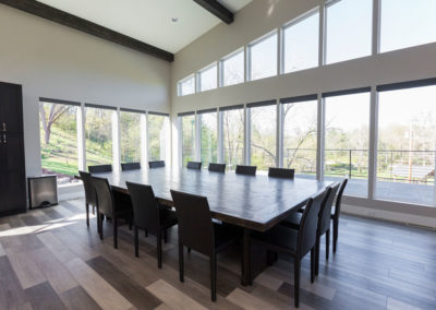Interior dining space with black dining table, modern chairs, extensive windows overlooking grounds, and contemporary design