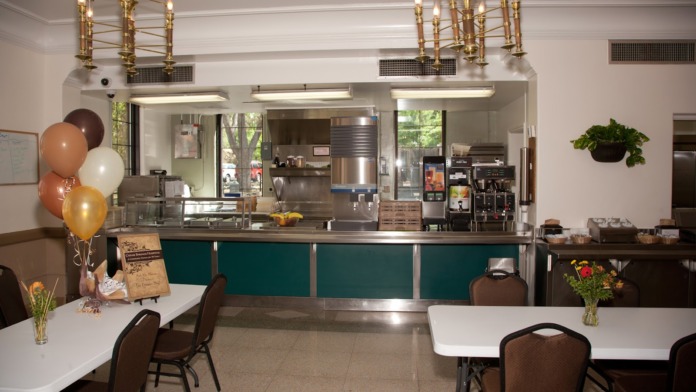Interior dining space with serving counter, commercial kitchen, tables with seating, and decorative balloon arrangements
