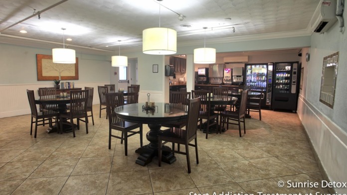 Interior dining area with multiple round black tables, wooden chairs, pendant lighting, and vending machines.