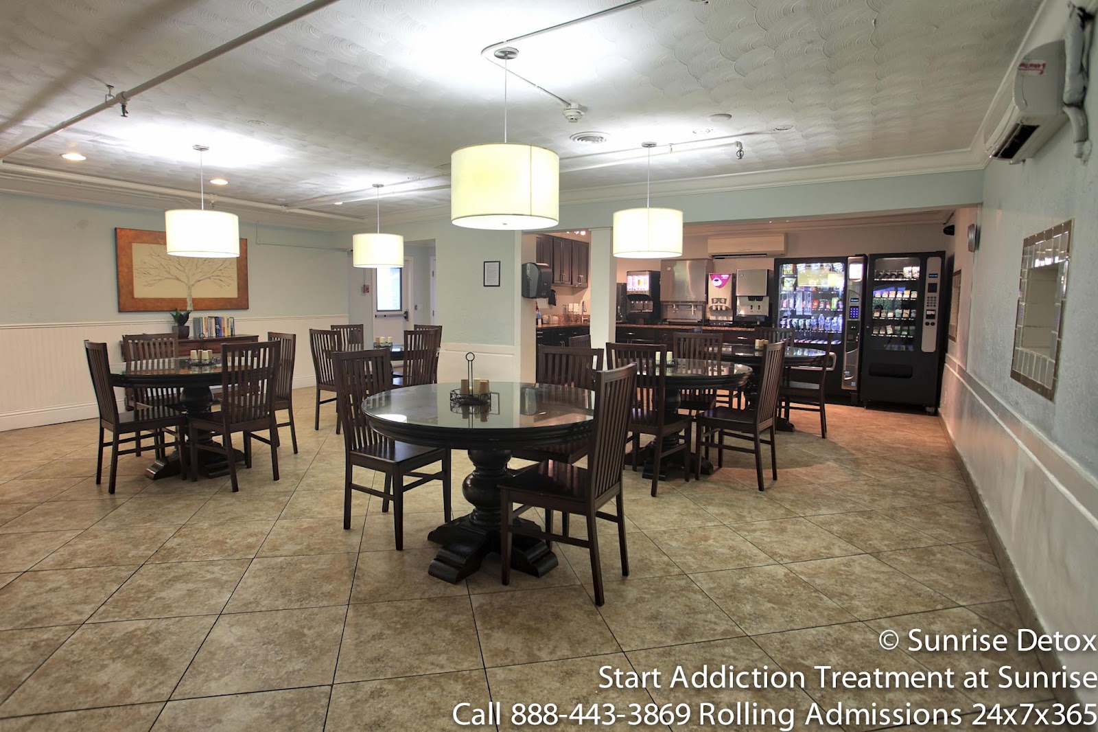 Interior dining area with multiple round black tables, wooden chairs, pendant lighting, and vending machines.