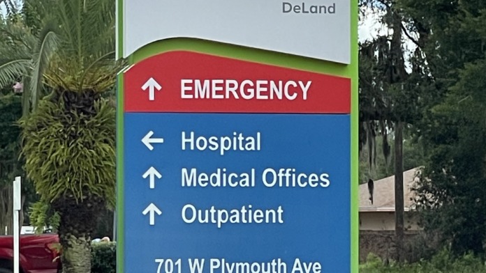 Outdoor wayfinding sign for AdventHealth DeLand showing emergency, hospital, medical office, and outpatient directions with address and landscaping
