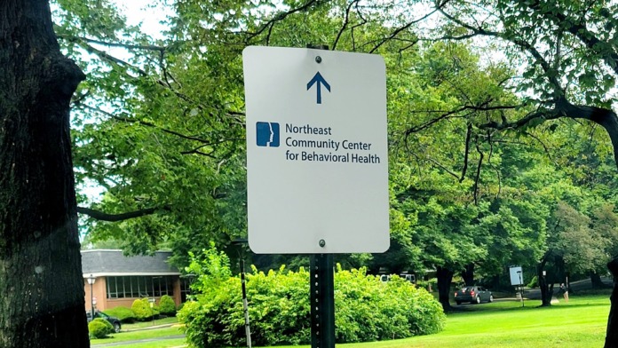 Outdoor directional sign with facility logo and upward arrow indicating parking and entrance directions surrounded by landscaping