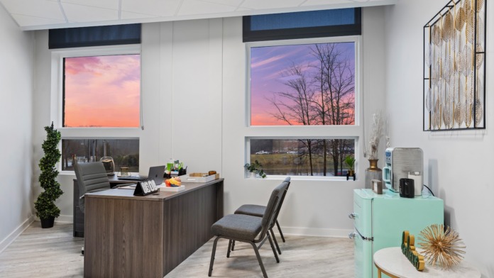 Interior office space with large windows showing sunset views, dark wood desk, and professional furnishings