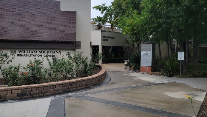 Exterior rehabilitation center building with brick signage, landscaped grounds, walkway entrance and surrounding vegetation
