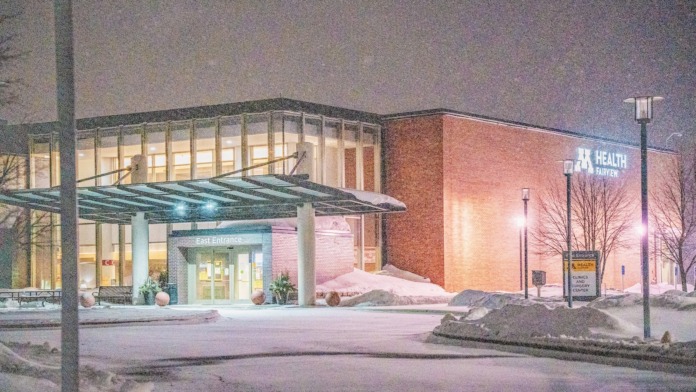 Exterior east entrance with glass pergola canopy, illuminated brick facade, landscaping, and winter snow coverage in evening light