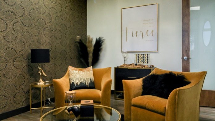 Interior lounge with golden upholstered armchairs, ornate chandelier, patterned wallpaper, and wall signage.