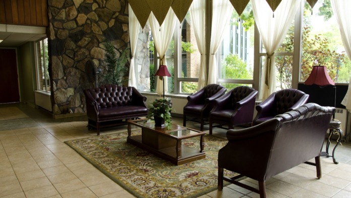Interior lounge with stone fireplace, purple leather seating, patterned rug, and natural light from windows