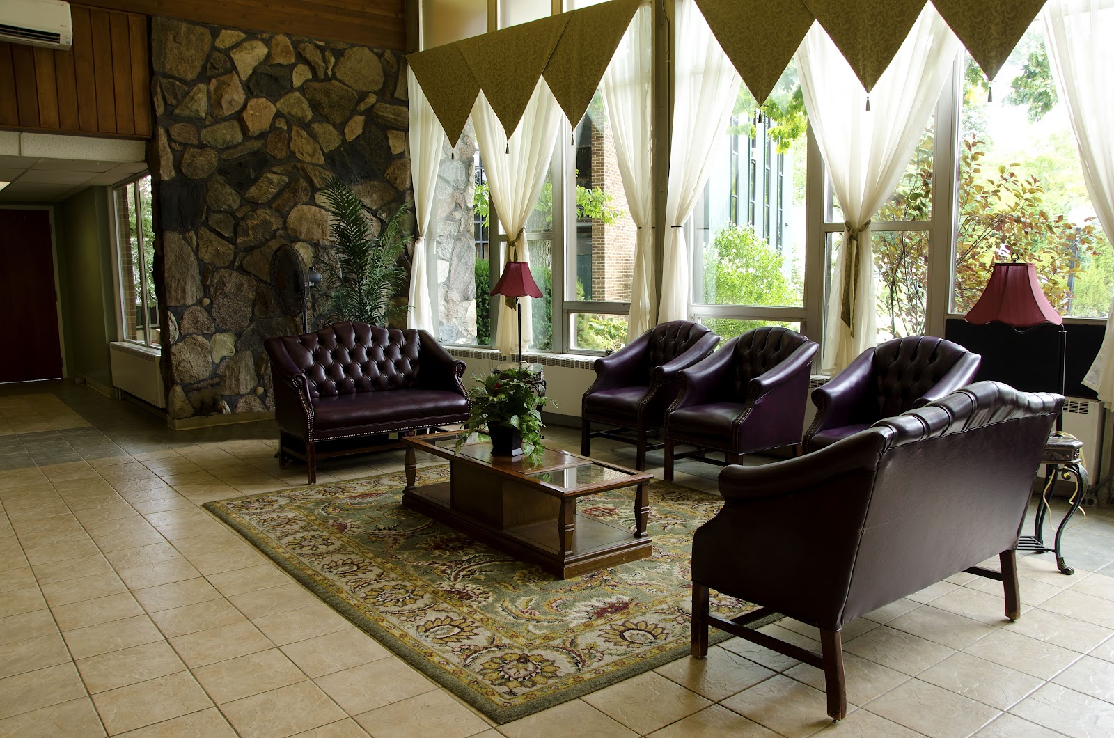 Interior lounge with stone fireplace, purple leather seating, patterned rug, and natural light from windows