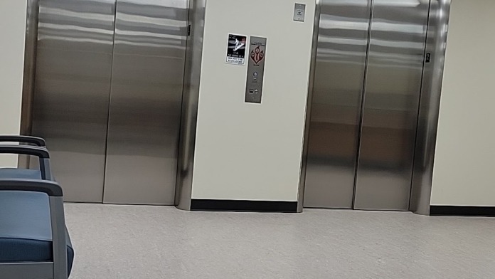 Interior showing two stainless steel elevators with waiting area and drop ceiling with modern fixtures