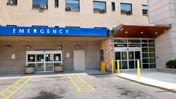 Exterior emergency department entrance showing blue signage, glass doors, and ambulance drop-off area with yellow markings
