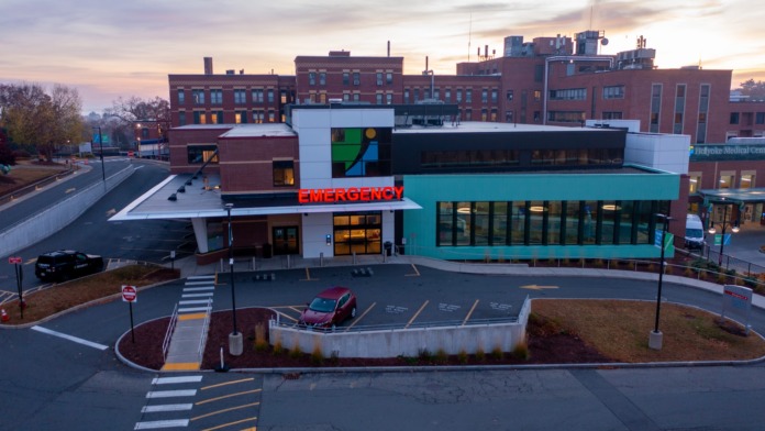 Exterior view of modern emergency department with turquoise facade, emergency signage, and covered entrance portico