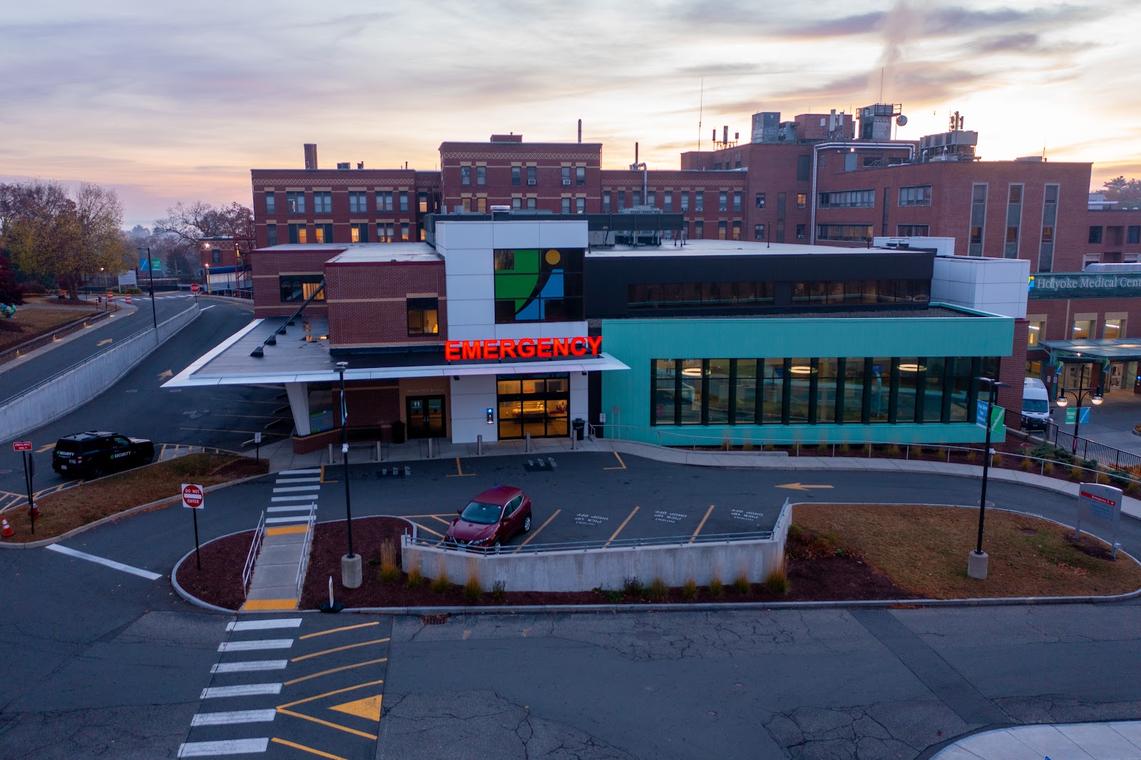 Exterior view of modern emergency department with turquoise facade, emergency signage, and covered entrance portico