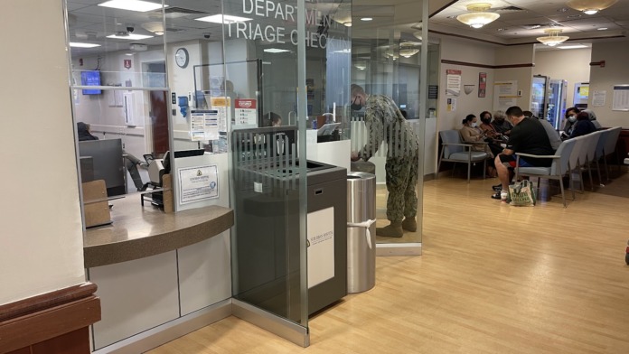 Interior emergency department with glass-enclosed triage counter, waiting seating area, and reception desk