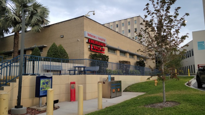 Exterior facility with red Emergency and blue Urgent care signage, brick facade, palm trees, and landscaping