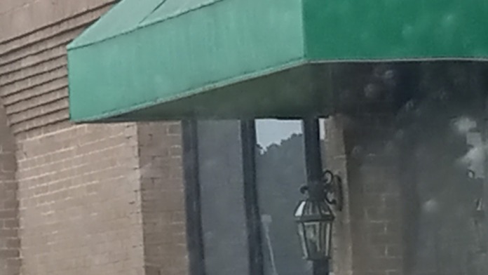 Close-up of teal green canvas awning, brick exterior wall, glass entry door, and landscaping