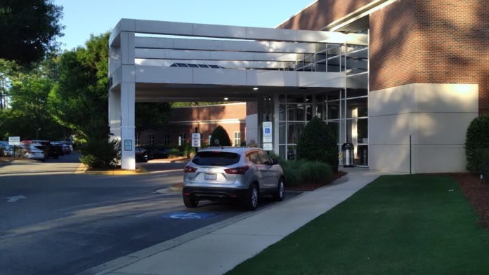 Exterior entrance covered area with glass doors, brick facade, landscaping, and parking area beneath modern canopy structure