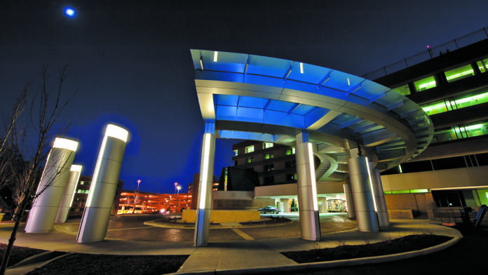 Exterior night view of hospital entrance with illuminated blue and white canopy structure, architectural lighting design
