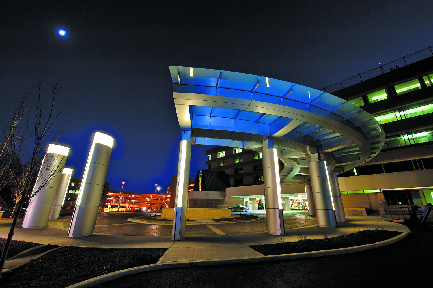 Exterior night view of hospital entrance with illuminated blue and white canopy structure, architectural lighting design