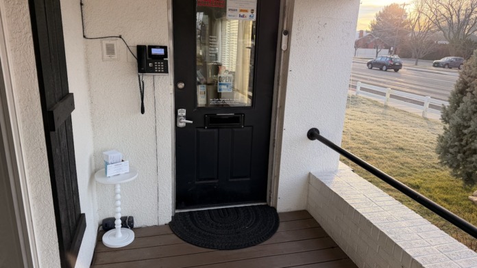 Exterior entry portico with black door, welcome mat, keypad entry system, and white railing overlooking landscaped grounds