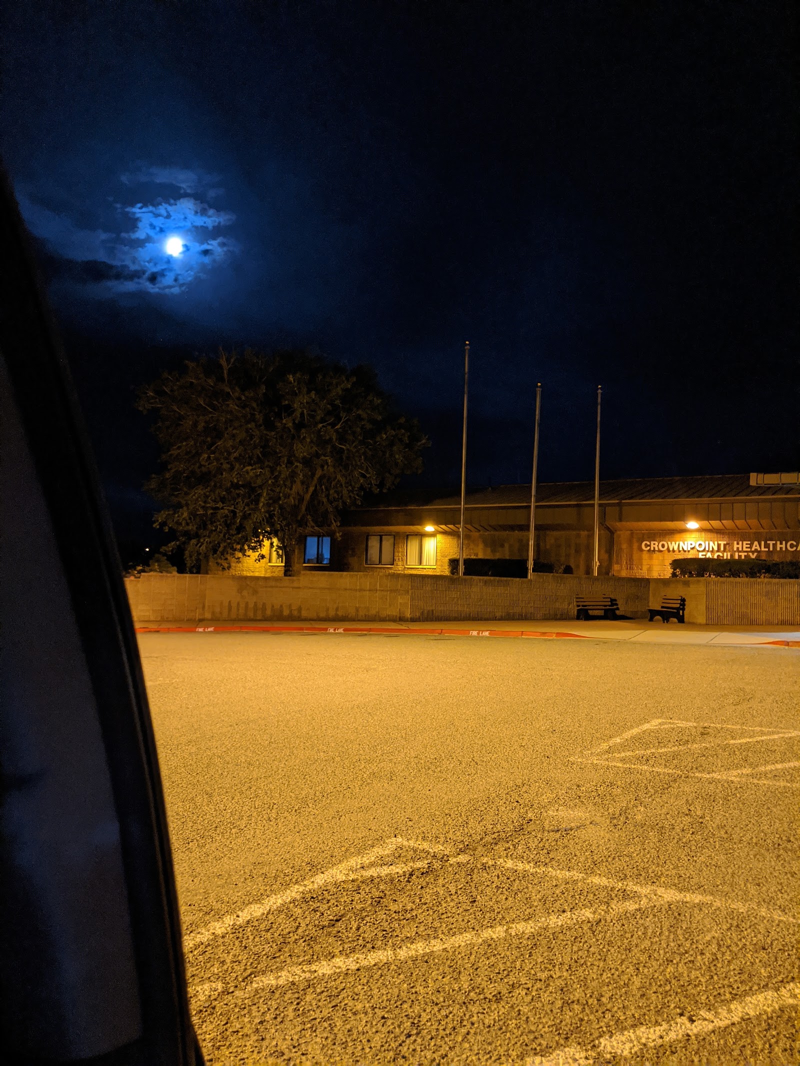 Exterior nighttime view of facility with parking area, illuminated building signage, and moonlit sky