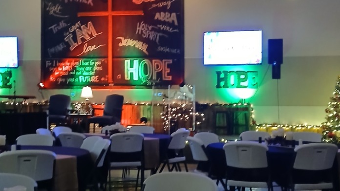 Interior gathering space with neon cross sign, decorative lighting, motivational wall displays, and seating