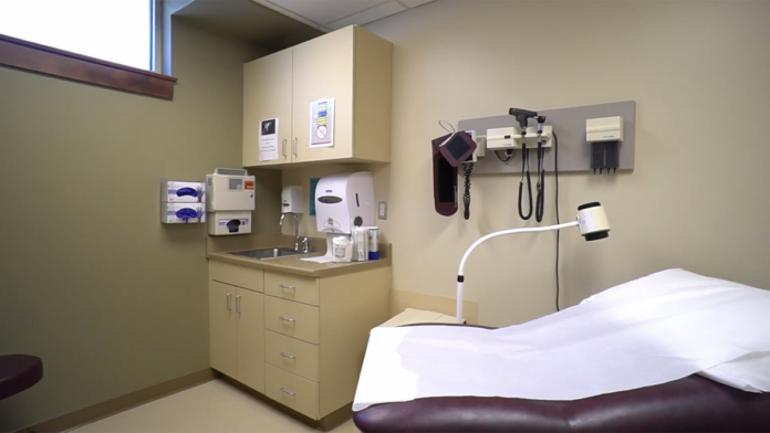 Interior medical examination room with examination table, sink, medical equipment on wall, and treatment supplies