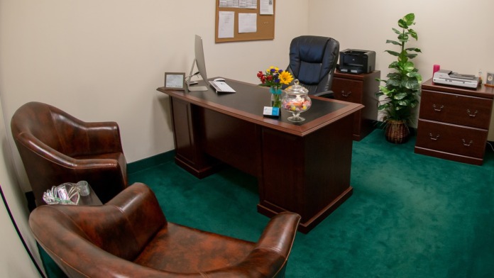 Interior office featuring mahogany desk with executive chair, leather seating, green carpeting, plants, and professional décor