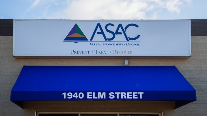 Exterior building entrance with ASAC logo signage, blue awning, address marking, brick facade, and entrance pathway