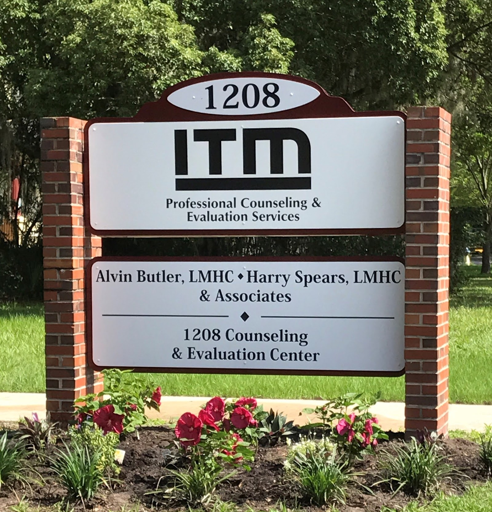 Exterior signage mounted on brick pillars displaying facility address number 1208 and business information with landscaping
