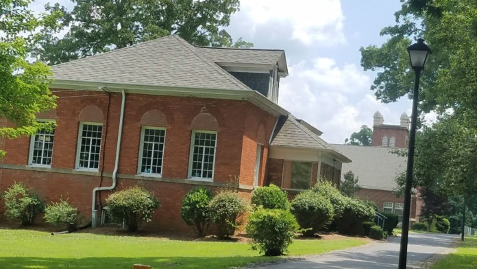Exterior of red brick building with gray roof, arched windows, manicured shrubs, and grounds lighting