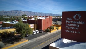 Exterior view of treatment facility campus showing brick buildings, parking area, palm trees, and mountain backdrop in Tucson