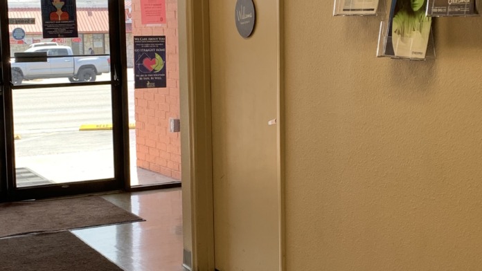 Interior hallway with beige walls, multiple doors leading to patient rooms or offices, fluorescent lighting, and clean tile flooring