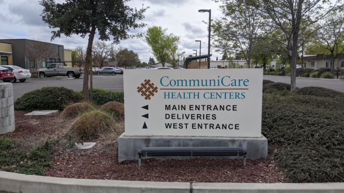 Exterior facility sign displaying Communicare Health Centers logo with directional arrows for main entrance, deliveries, and west entrance among landscaped grounds