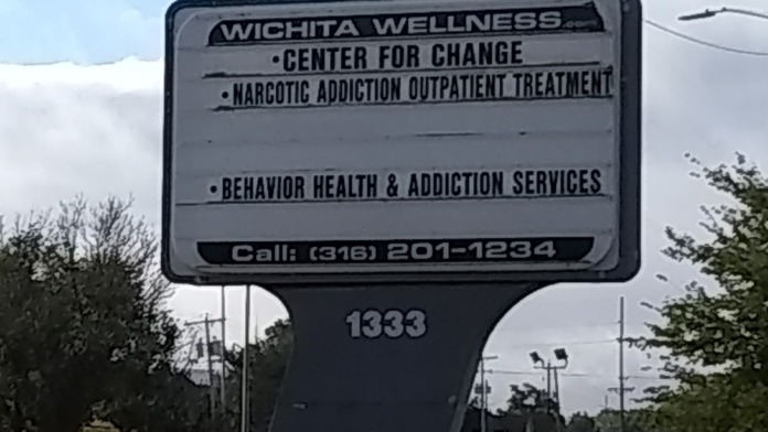 Roadside directional sign for Wichita Wellness Center for Change listing treatment services and contact phone number