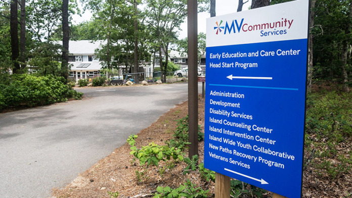 Exterior wayfinding sign with MV Community Services branding and program directory with building in background