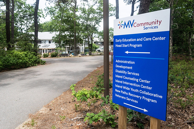 Exterior wayfinding sign with MV Community Services branding and program directory with building in background