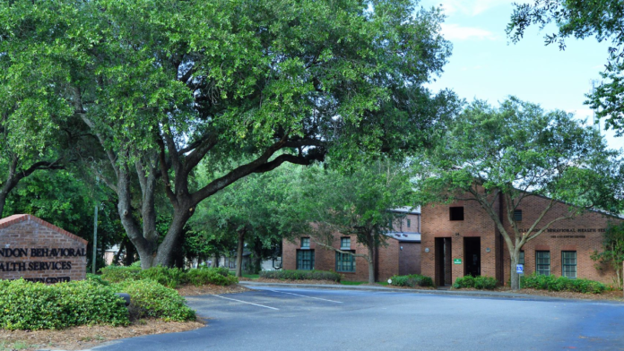Exterior entrance area with Clarendon Behavioral Health Services sign, mature trees, and facility grounds leading to brick building