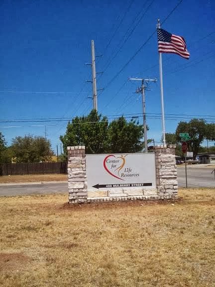Exterior facility sign for Center for Life Resources with American flag, landscaped grounds, and clear blue sky