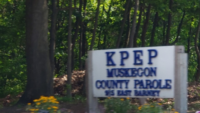 Exterior facility sign for KPEP Muskegon County Parole with landscaped gardens and tall trees.