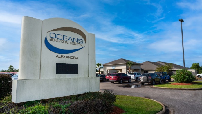 Exterior signage displaying Oceans Behavioral Hospital Alexandria name with parking lot and facility building in background