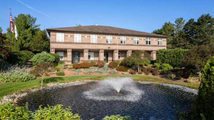 Brick facility building with American flag, stone landscaping accents, water feature, and clear sky