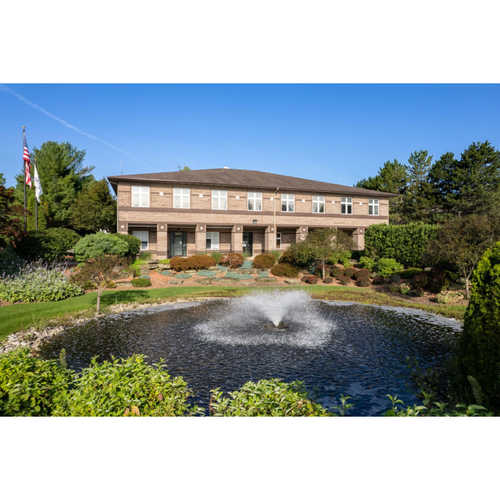 Brick facility building with American flag, stone landscaping accents, water feature, and clear sky