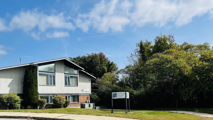 Exterior view of healthcare facility from parking area showing main entrance, signage, and surrounding landscape