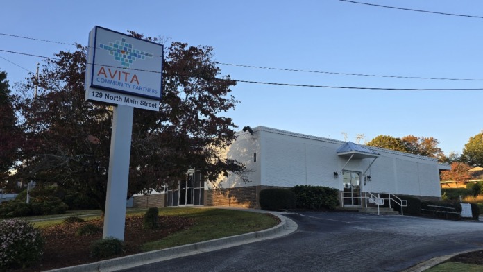 Exterior view of behavioral health facility with Avita Community Partners sign displaying address 129 North Main Street, white brick building with entrance visible